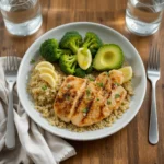 A balanced plate featuring grilled chicken, quinoa, steamed broccoli, and sliced avocado, for healthy eating served on a white plate with a fork and napkin beside it